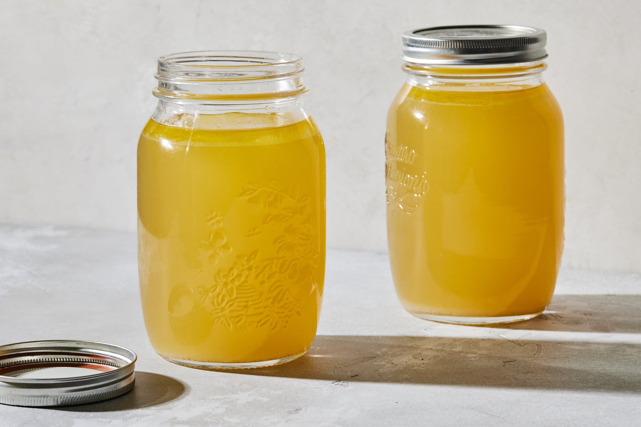 Two Mason jars filled with chicken broth are photographed from the side. 