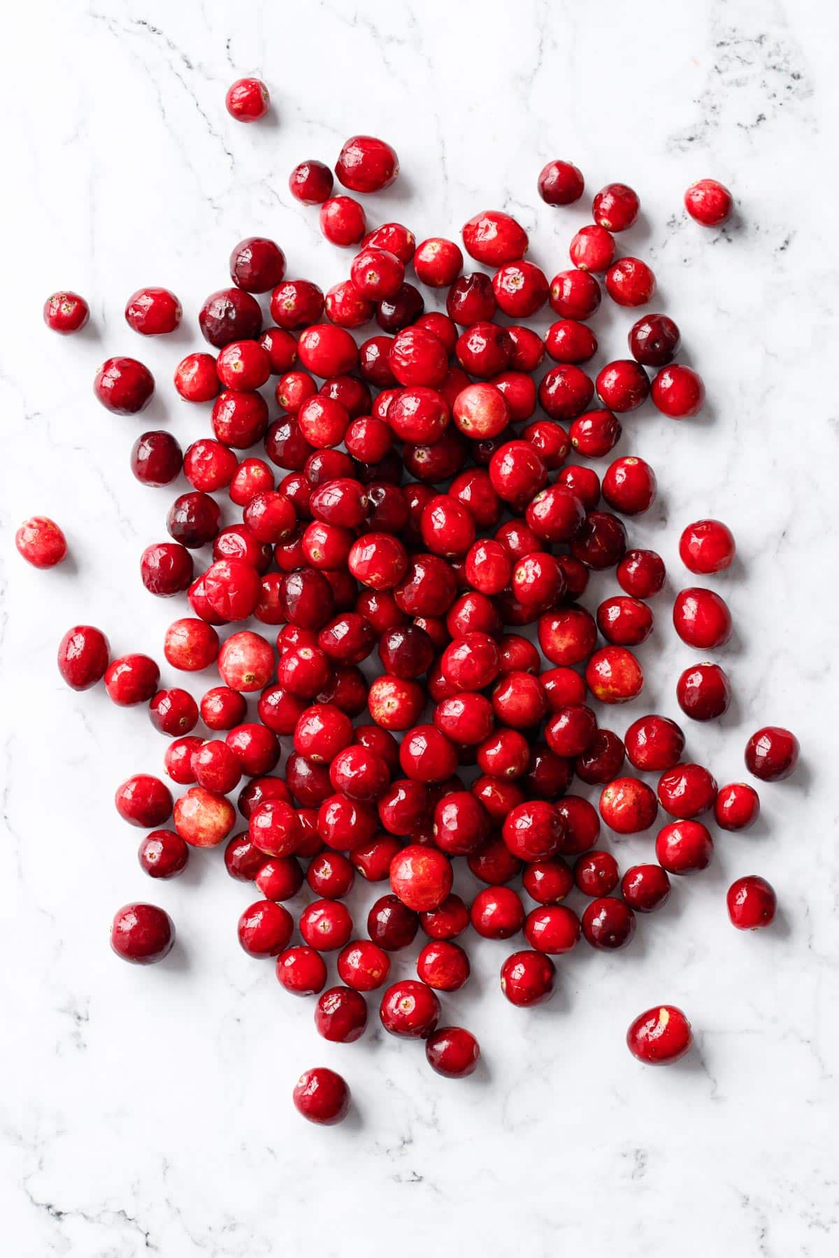 Pile of fresh cranberries scattered on a marble surface with an overhead perspective.