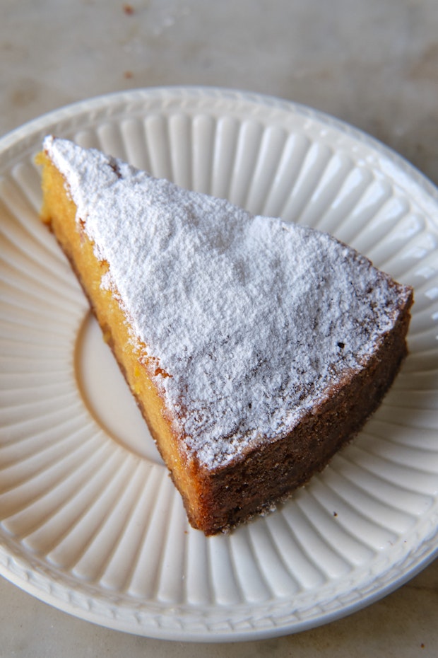 a slice of almond cake dusted with powdered sugar on a white plate