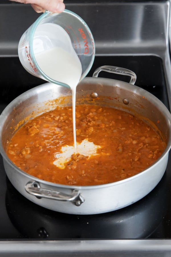 Pouring cream into saucepan with tomato-based sauce.