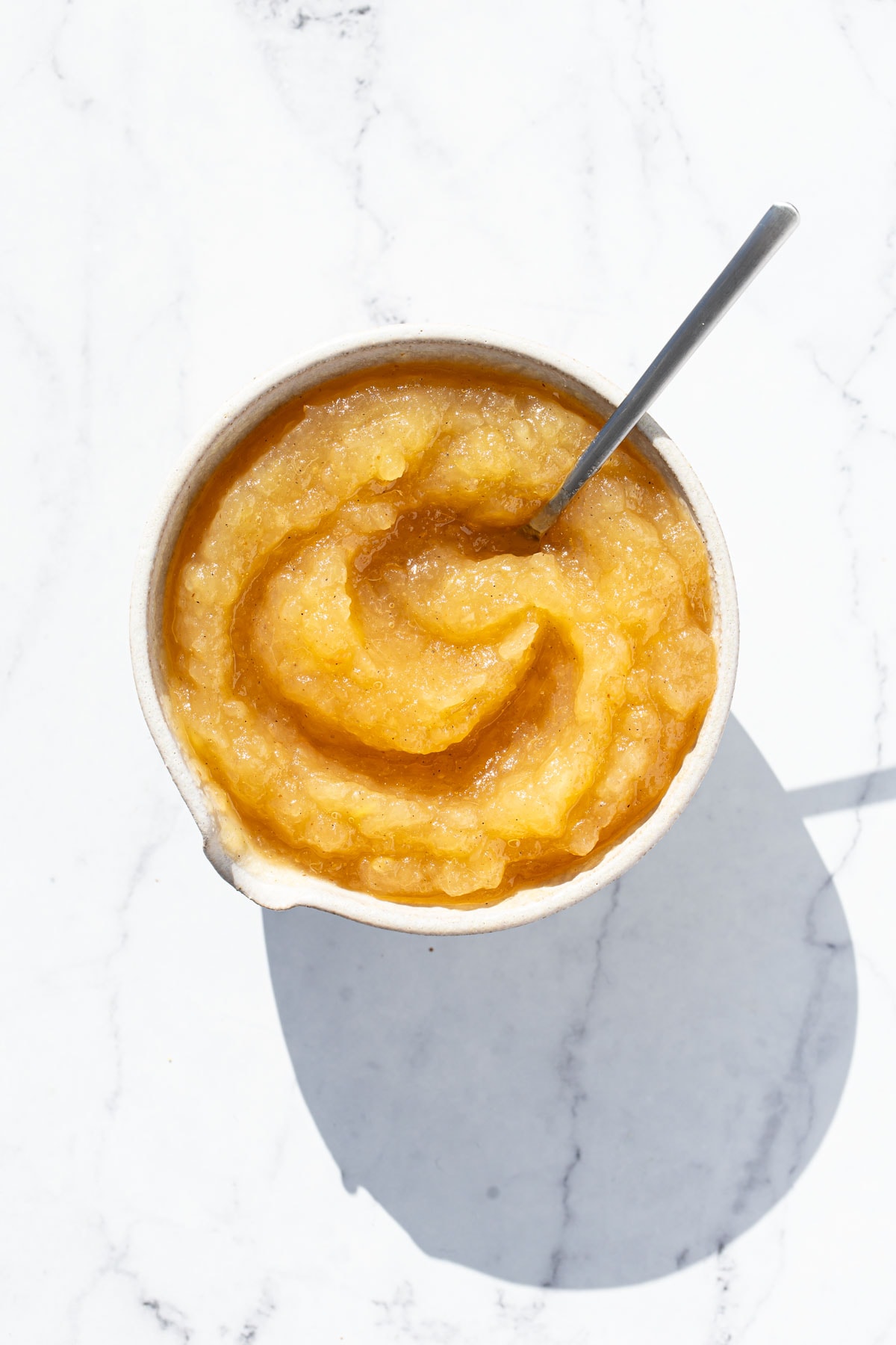 Overhead perspective, white bowl with a swirl of homemade applesauce and a spoon sticking out of it.