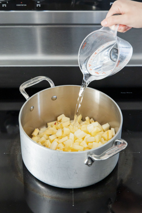 Pouring water into saucepan with apples and lemon juice.