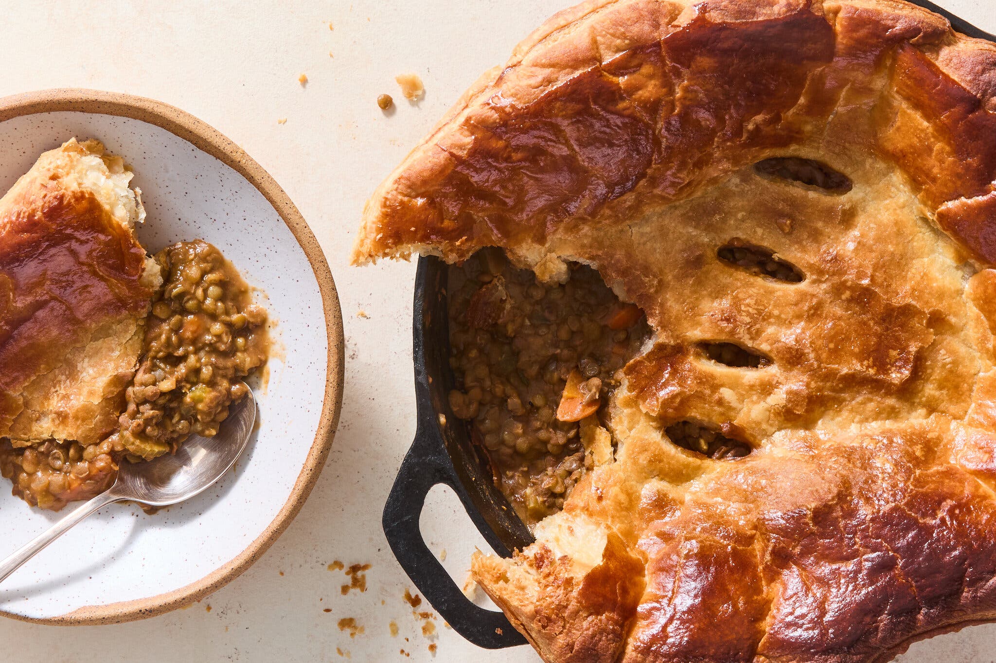 An overhead image of a skillet filled with lentil soup and topped with puff pastry.