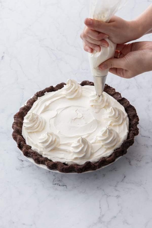 Piping florets of whipped cream on top of the cream-topped pie.