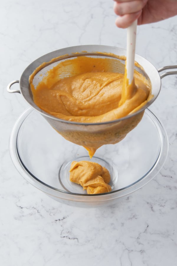 Pressing cooked custard through a fine mesh sieve to strain out any stray lumps.