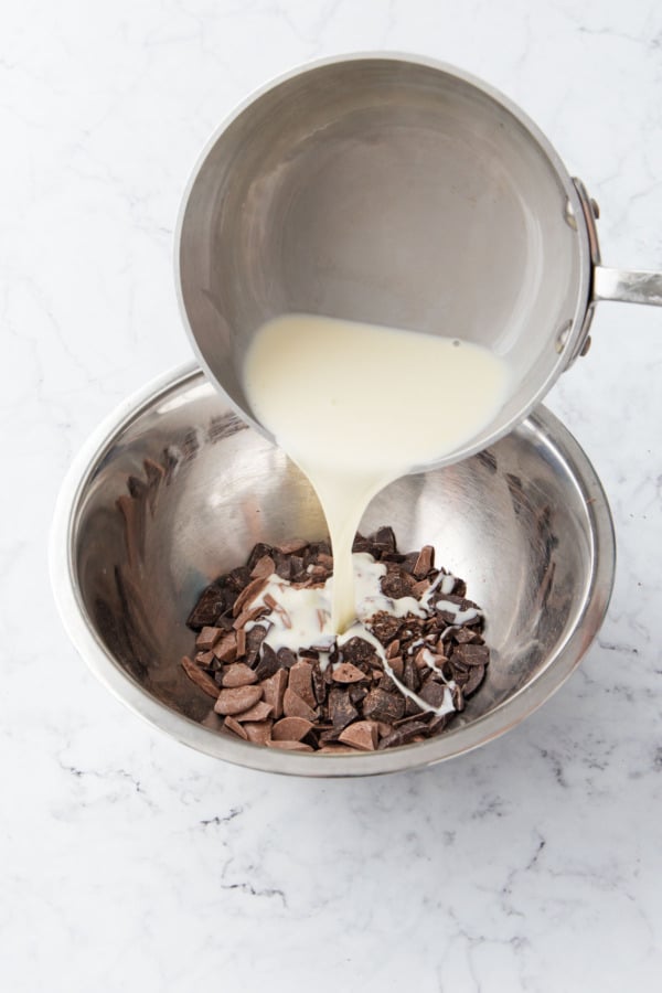 Pouring hot cream into a bowl with chopped chocolate.